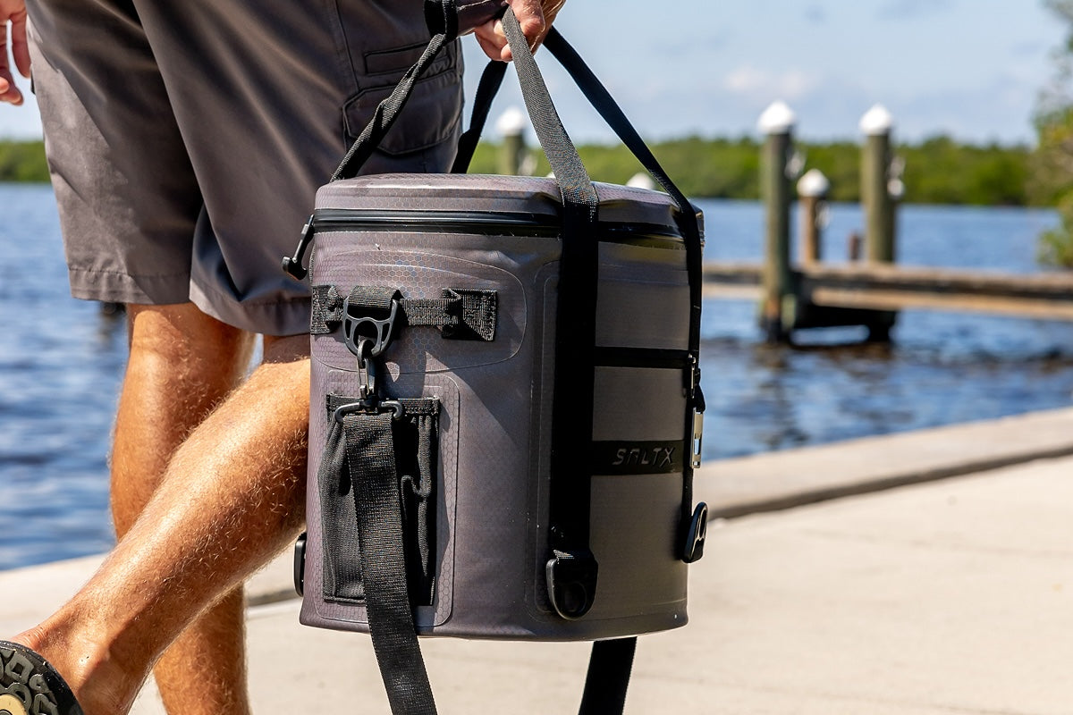 Person carrying a gray cooler bag by a waterfront