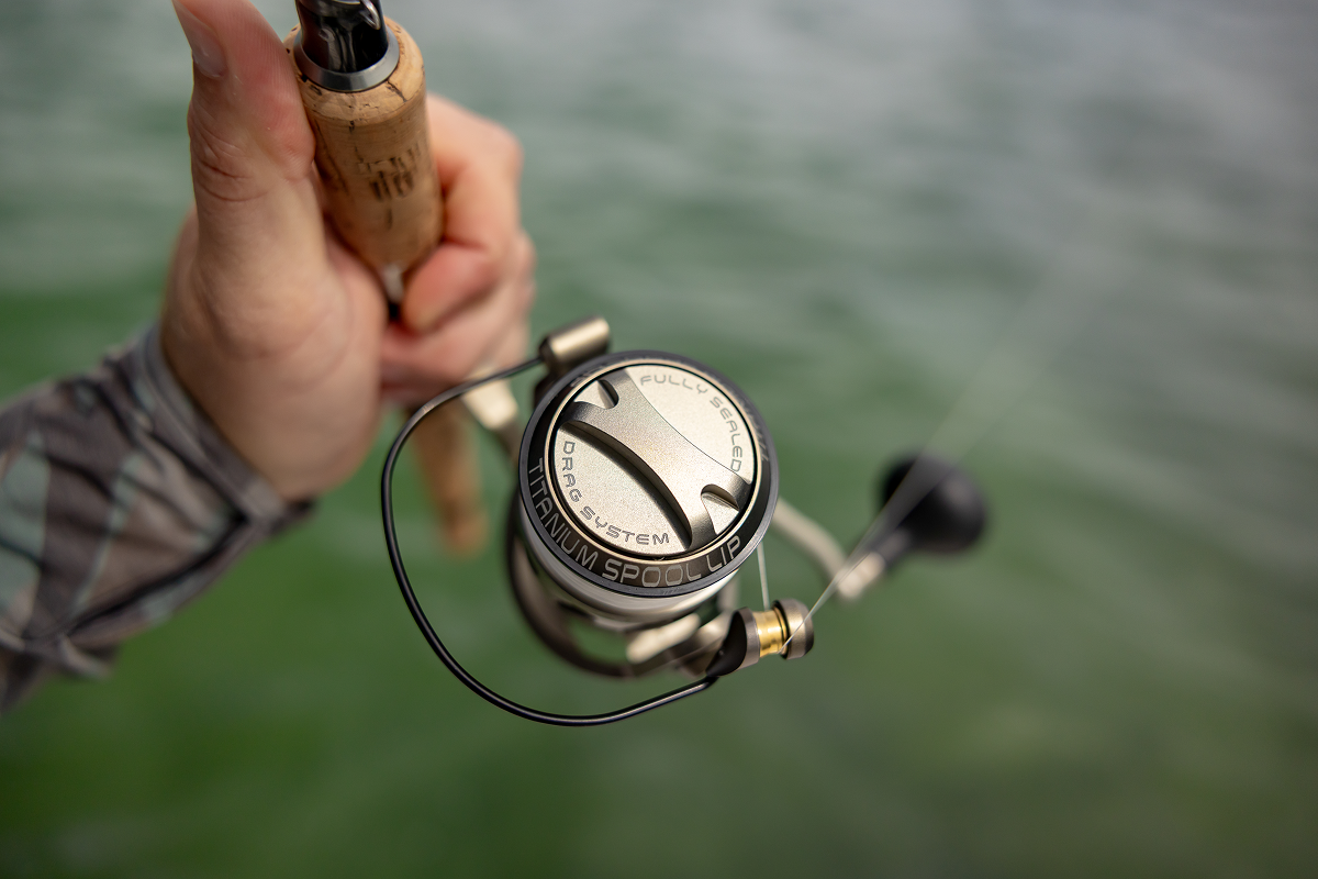 Fishing reel held by a hand with blurred water background