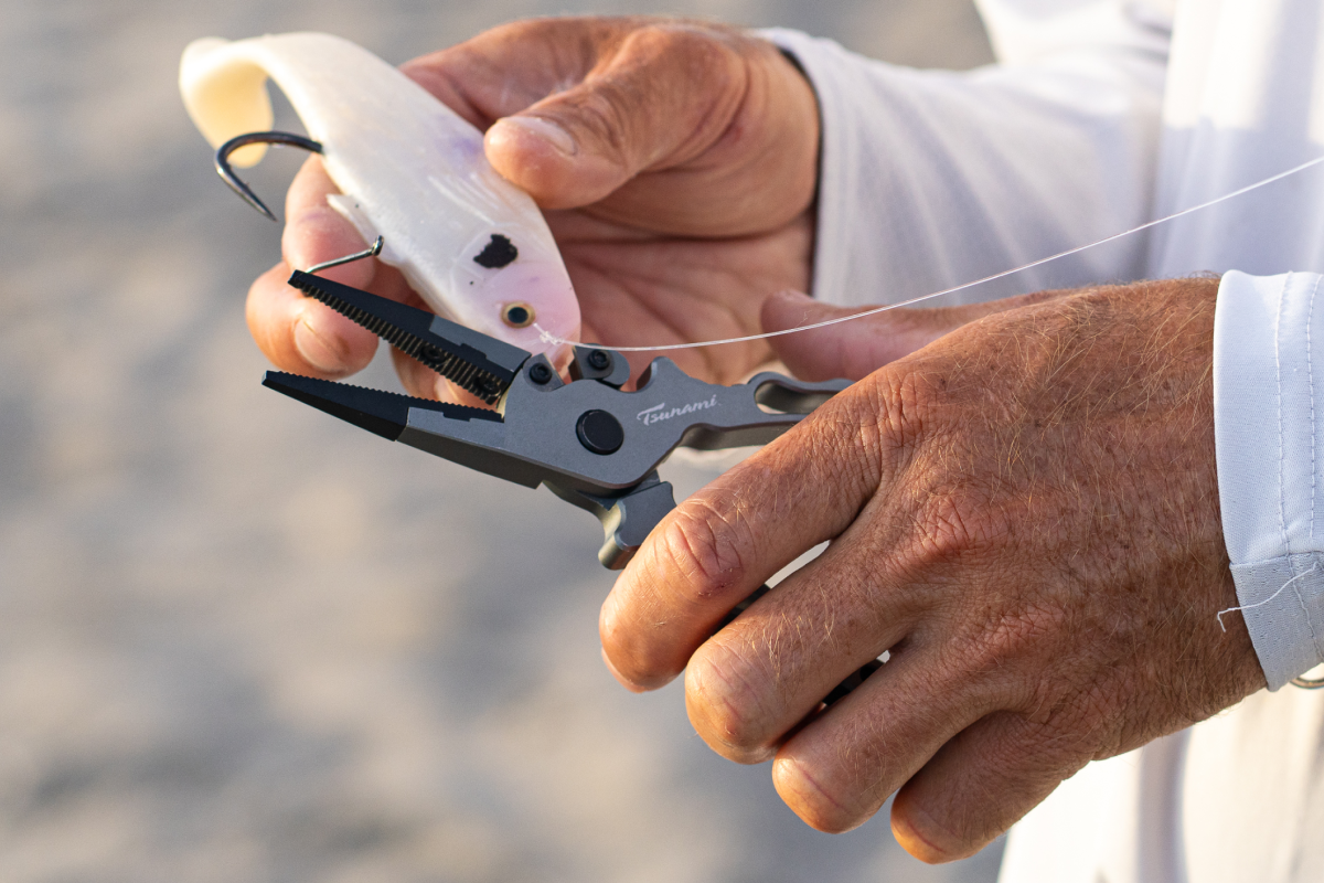 Person using a plier tool to cut fishing line on a beach.