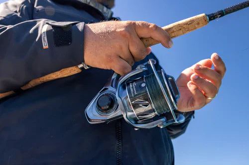 Close-up of a hand holding a fishing reel with a clear blue sky background